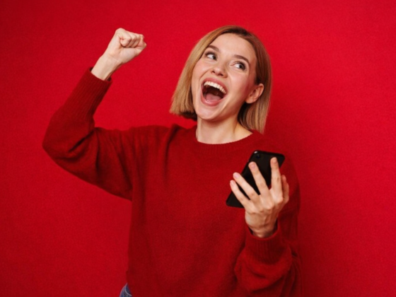 Mulher comemora com o celular na mão após conferir resultado de aposta online, simbolizando ganhador da Mega-Sena