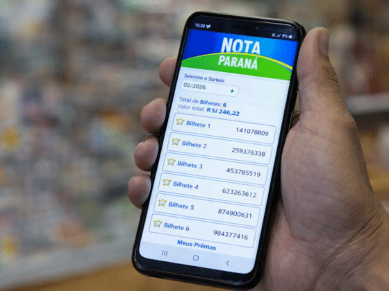 Pessoa segura um smartphone com o aplicativo Nota Paraná aberto, mostrando bilhetes do sorteio e valores acumulados na tela.