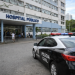 Viatura da polícia estacionada na entrada de hospital público no Rio de Janeiro, com circulação moderada de pessoas durante o dia