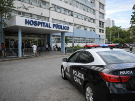 Viatura da polícia estacionada na entrada de hospital público no Rio de Janeiro, com circulação moderada de pessoas durante o dia