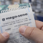 Close-up de bilhete da Mega-Sena com aviso de combate ao assédio impresso, segurado por apostador em ambiente iluminado