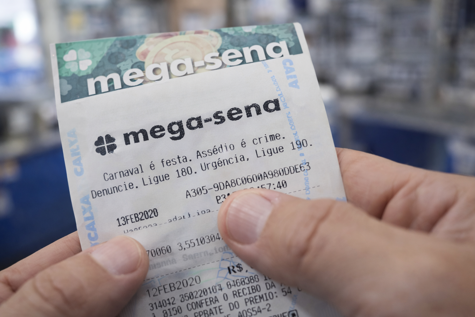 Close-up de bilhete da Mega-Sena com aviso de combate ao assédio impresso, segurado por apostador em ambiente iluminado