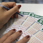 Pessoa marcando números em volantes da Mega-Sena com caneta azul sobre balcão, em close-up durante aposta
