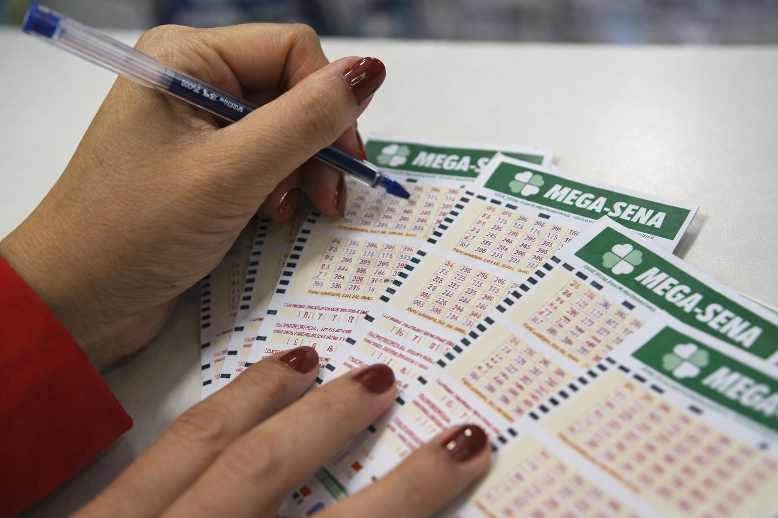 Pessoa marcando números em volantes da Mega-Sena com caneta azul sobre balcão, em close-up durante aposta
