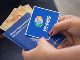 Mãos segurando cartão do PIS/Pasep junto a carteira de trabalho e dinheiro em real, representando pagamento do abono salarial no Brasil