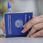 Mão segurando carteira de trabalho azul sobre mesa, representando mercado de trabalho e vínculos formais no Brasil