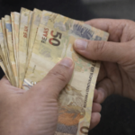 Mãos segurando e contando notas de 50 reais, representando pagamento, renda e movimentação financeira no Brasil