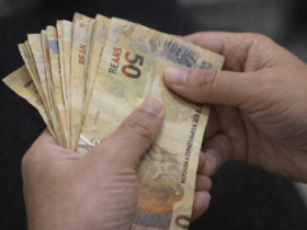 Mãos segurando e contando notas de 50 reais, representando pagamento, renda e movimentação financeira no Brasil