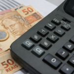 Calculadora ao lado de notas de 50 reais e moeda, representando cálculo de impostos, herança e planejamento financeiro no Brasil