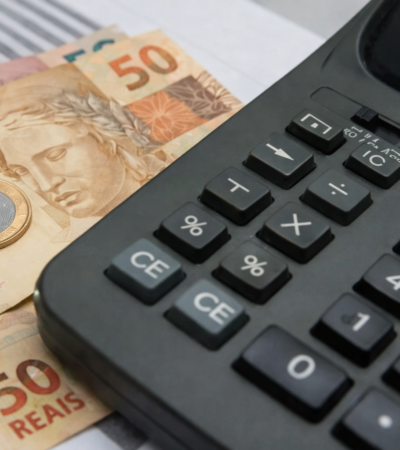 Calculadora ao lado de notas de 50 reais e moeda, representando cálculo de impostos, herança e planejamento financeiro no Brasil