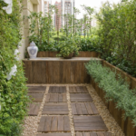 Pequeno jardim em varanda com parede verde, vasos e piso de madeira, exemplo de paisagismo para espaços reduzidos em apartamento.