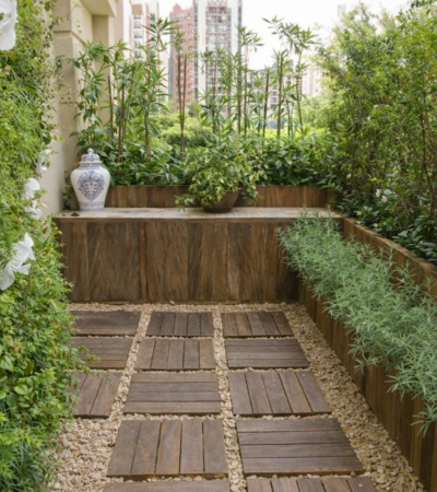 Pequeno jardim em varanda com parede verde, vasos e piso de madeira, exemplo de paisagismo para espaços reduzidos em apartamento.