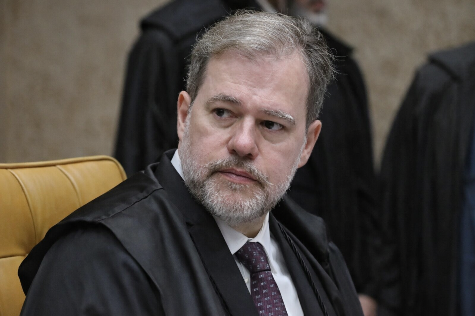 Ministro Dias Toffoli em sessão do STF, usando toga preta e gravata vinho, sentado em plenário com outros magistrados ao fundo.