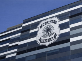 Prédio moderno da Polícia Federal com brasão da corporação estampado na fachada envidraçada sob céu azul.