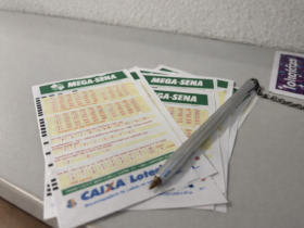 Volantes da Mega-Sena com caneta apoiada sobre os bilhetes em casa lotérica, representando aposta para prêmio milionário