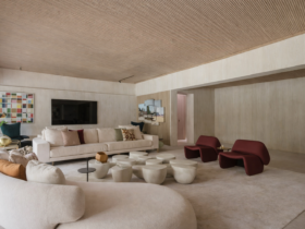 Sala de estar contemporânea com sofá curvo claro, poltronas vermelhas e mesas de centro esculturais em ambiente com teto de madeira e iluminação natural