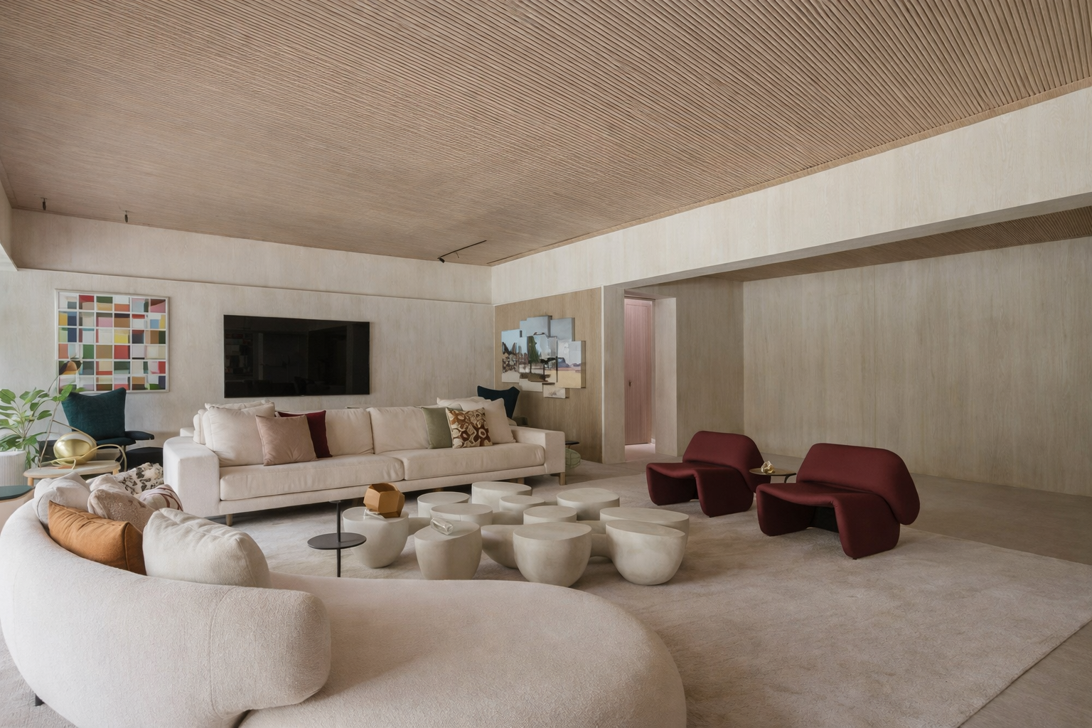 Sala de estar contemporânea com sofá curvo claro, poltronas vermelhas e mesas de centro esculturais em ambiente com teto de madeira e iluminação natural