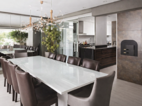 Sala de jantar moderna integrada à varanda gourmet com mesa branca, cadeiras de couro marrom, portas de vidro deslizantes e iluminação pendente sofisticada.