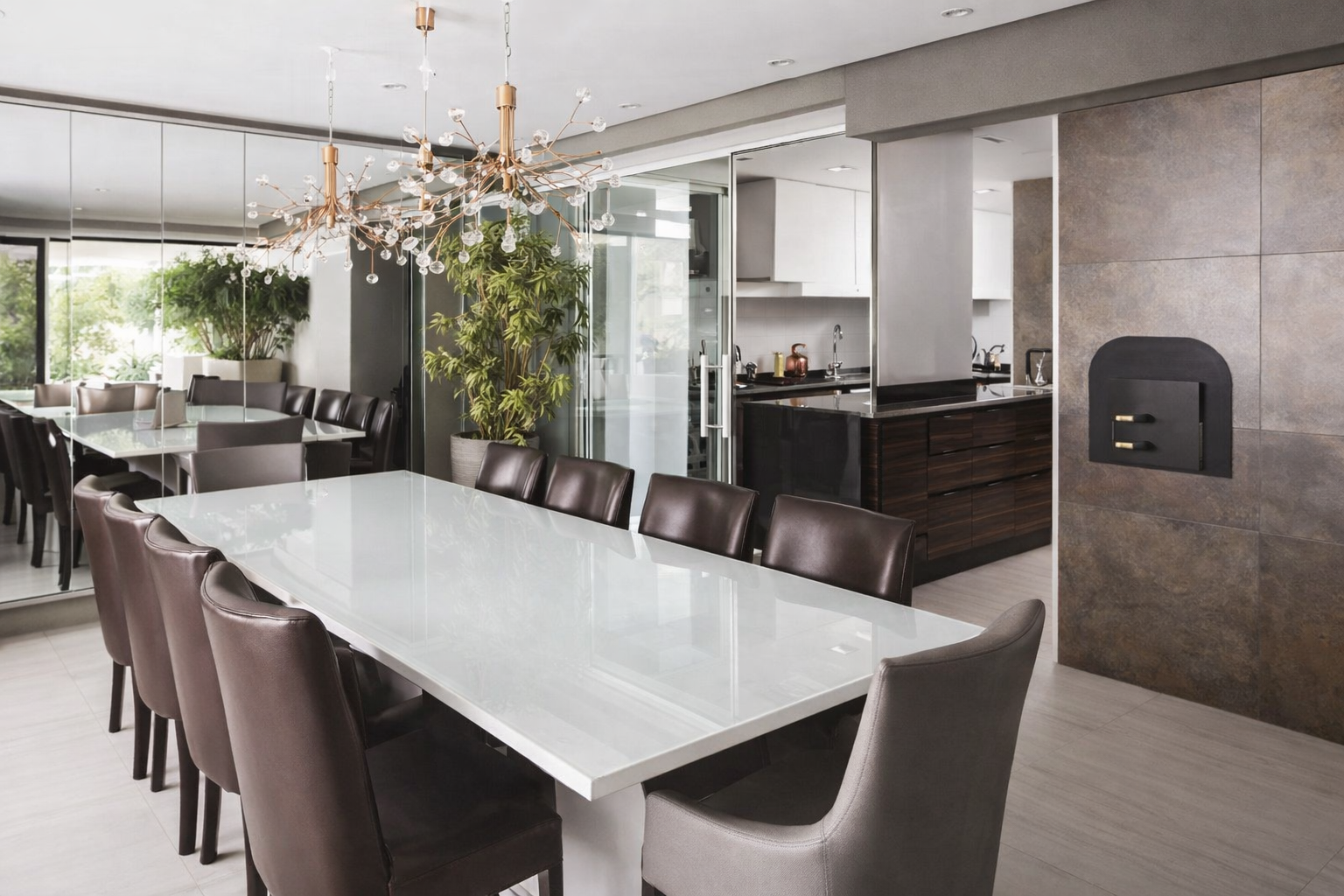 Sala de jantar moderna integrada à varanda gourmet com mesa branca, cadeiras de couro marrom, portas de vidro deslizantes e iluminação pendente sofisticada.