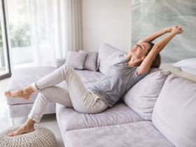 Mulher relaxando no sofá em sala clara e ventilada, com luz natural entrando pela janela e ambiente minimalista aconchegante.