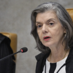Cármen Lúcia fala ao microfone em sessão do TSE, sentada em cadeira do plenário com toga preta