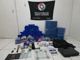 Tabletes de maconha, balanças de precisão, celulares e colete tático apreendidos pela Polícia Militar de Santa Catarina exibidos em sala oficial