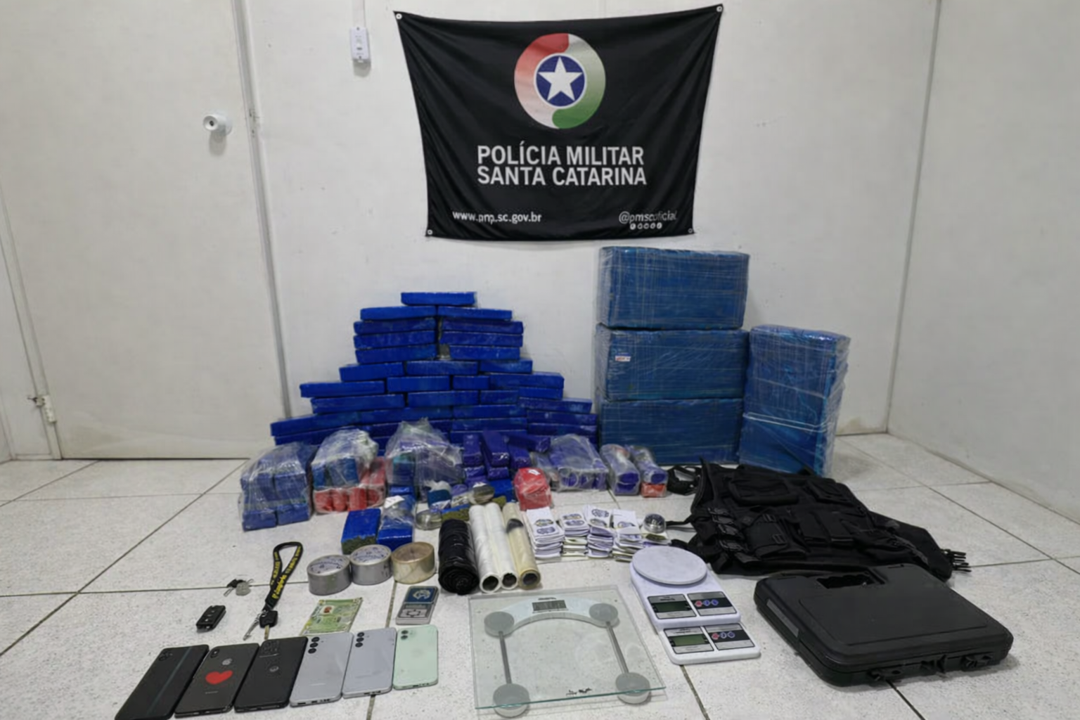 Tabletes de maconha, balanças de precisão, celulares e colete tático apreendidos pela Polícia Militar de Santa Catarina exibidos em sala oficial