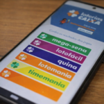 Celular com aplicativo Loterias Caixa aberto mostrando Mega-Sena, Lotofácil e Quina na tela.