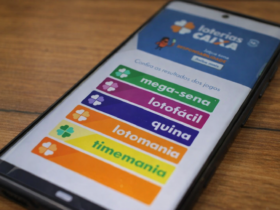 Celular com aplicativo Loterias Caixa aberto mostrando Mega-Sena, Lotofácil e Quina na tela.