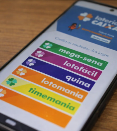 Celular com aplicativo Loterias Caixa aberto mostrando Mega-Sena, Lotofácil e Quina na tela.
