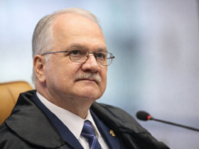 Retrato em três quartos do ministro Edson Fachin no plenário do STF, usando toga, gravata azul e sentado em cadeira marrom com microfone ao lado.