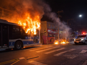 Dois ônibus urbanos incendiados na zona sul de São Paulo, com chamas altas, fumaça intensa e viatura policial ao lado da via.