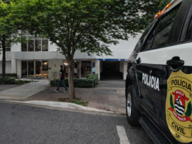 Entrada de prédio comercial em Moema, São Paulo, com fachada branca, árvore em frente e pedestre caminhando na calçada.