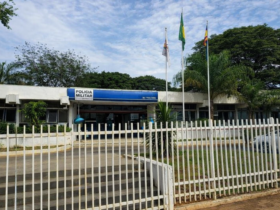 Fachada de unidade da Polícia Militar em Curvelo, Minas Gerais, com bandeiras hasteadas e grade branca na parte frontal do prédio.