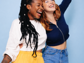 Duas mulheres jovens sorrindo e abraçadas diante de fundo azul, representando amizade, diversidade e alegria