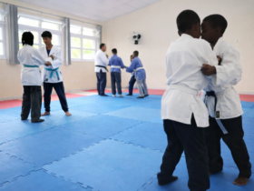 Estudantes treinando judô em sala com tatame durante projeto de contraturno escolar em ambiente educativo.