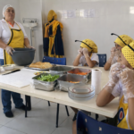 Crianças participando de oficina de preparo de alimentos em cozinha educativa de projeto social comunitário.