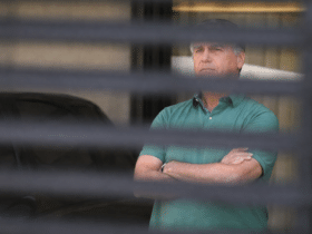 Bolsonaro visto através de persiana em imagem que simboliza acompanhamento médico e momento de incerteza política no Brasil